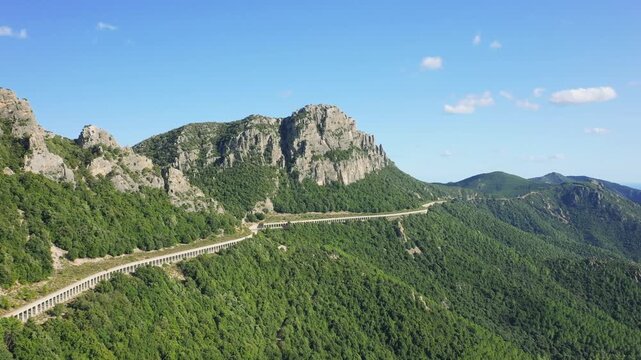 Aerial footage showing a winding road through lush green hills and rocky mountains in the countryside surrounding Baunei, Sardinia, Italy.