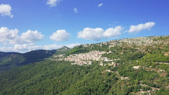 Aerial footage showing the picturesque village of Baunei surrounded by lush green hills and dramatic limestone cliffs in Sardinia, Italy.