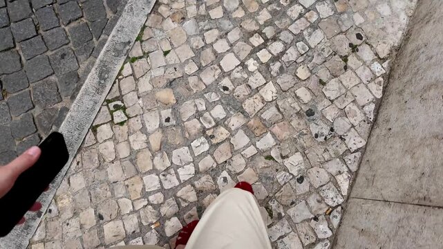 Woman Walking on Cobblestone Sidewalk Wearing White Loose Pants and Red Sandals