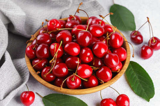 Fresh ripe red sweet cherries in wooden bowl with green leaves on light textured background. Healthy organic summer fruit, juicy red berries, natural freshness, healthy eating, seasonal food