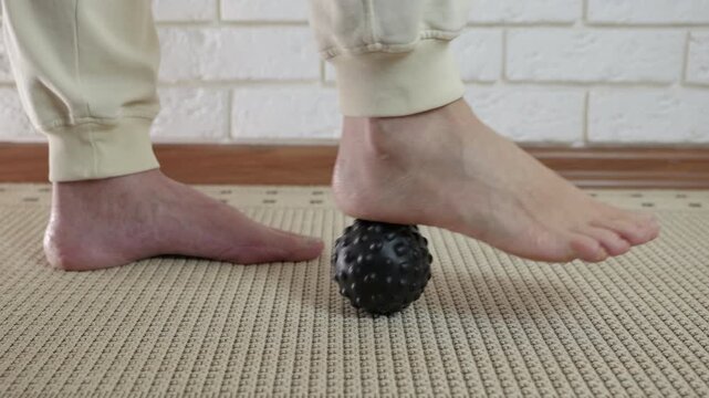Person massaging foot with spiky ball. Barefoot man rolling his foot on a spiky massage ball for trigger point therapy and myofascial release, helping to relieve pain from plantar fasciitis