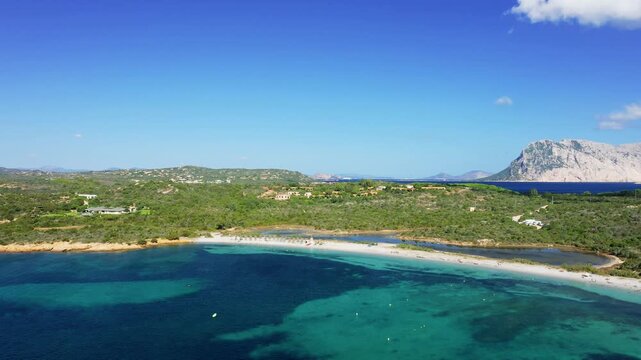 Aerial footage of Spiaggia la Salinedda beach in San Teodoro, Sardinia, Italy. The clear sky and calm sea create a picturesque coastal landscape, typical of northern Sardinia.