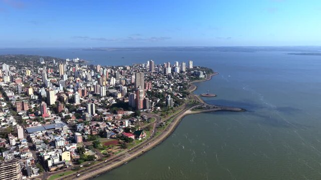 Aerial cityscape of Posadas skyline curving along the Parana River shoreline.