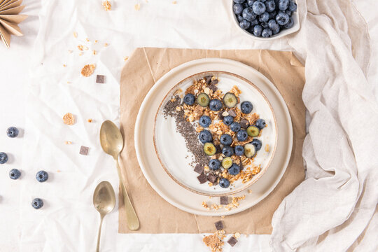 Healthy breakfast bowl with yogurt granola blueberries and chia seeds served in a rustic dish for a nutritious start to the day on white fabric