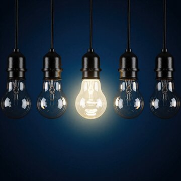 One light bulb glows brightly among unlit ones on a dark background. Concept represents unique idea, innovation, or standout solution in a group.