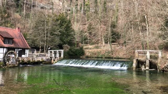 Riverside dam cascade by small mill with green pool and rippling surface under soft daylight, with water, cascade, river, dam detail, showing flow, ripple, foam, pool context