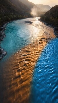 Aerial view of confluence where two rivers of different colored turquoise and golden water meet in mountain valley at sunrise, nature contrast and convergence concept