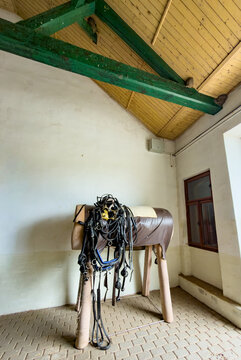 Horse training equipment is in a barn. A horse training dummy stands in a barn with equipment hung on it. The space has wooden beams and stone floor.