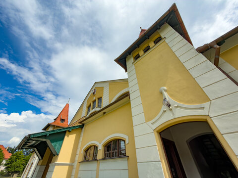 Building in blue sky with white clouds. A building with a yellow exterior under a blue sky filled with clouds. The building has distinct features.