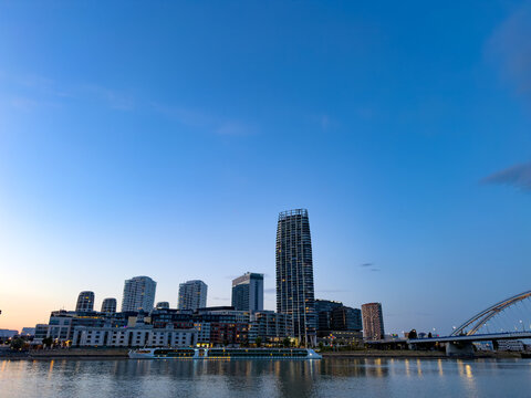 Dusk skyline by the water. A view of the city skyline at dusk shows modern buildings near the water. Some lights start to shine in the evening.