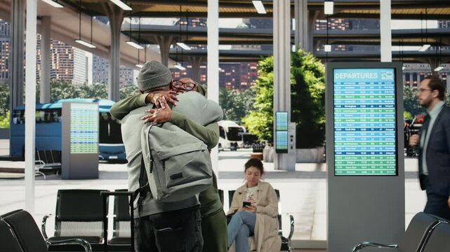 Smiling passengers hug in a bus terminal, happy to see each other again as friends meet in the coach terminal and enjoy an affectionate conversation.