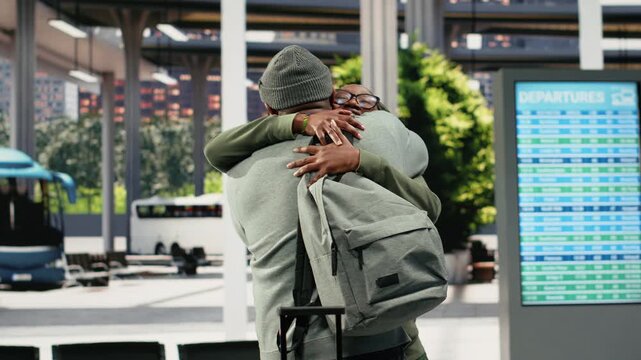 Smiling passengers hug in a bus terminal after seeing each other again, catching up in conversation as happy friends meet in the coach terminal.