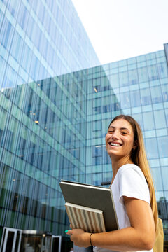 Happy young student carrying books on modern campus