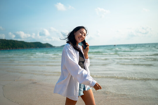 Happy woman celebrating freedom holding white shirt in the wind against blue sky at tropical beach