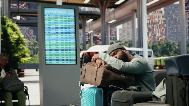 Weary traveler dozes on a trolley in a bus terminal from travel fatigue, resting on luggage during a long wait caused by a missed bus connection.
