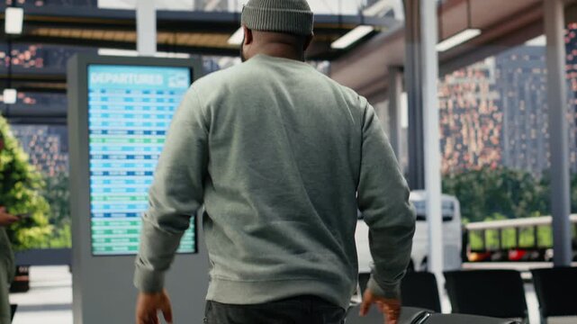 Passengers check an electronic timetable in a busy bus terminal during delays, reading the departure board schedule while annoyed by long waiting times.