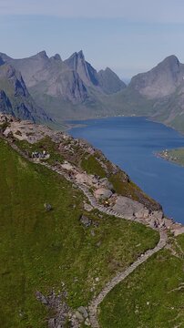 Aerial view of people hiking along stone steps on Reinebringen mountain ridge above Reinefjorden in Lofoten Islands Norway during a sunny day.