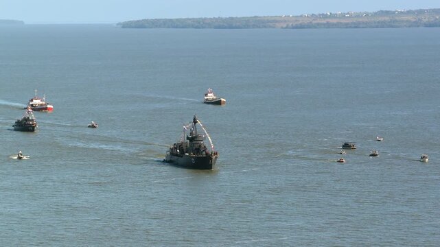 Military ship and patrol vessel sailing in formation with escort boats on the Parana River.