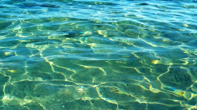 Sunlit turquoise ocean water surface with shimmering caustic light reflections and gentle rippling waves. Pure tropical sea background.