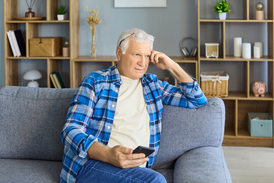 Senior man with smartphone on sofa at home. He relaxes in the living room, reading messages on his phone and using technology for easy communication. Clear concept of digital senior lifestyle.
