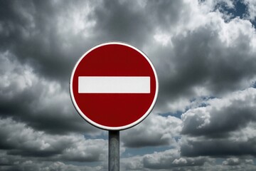 Fototapeta premium Red no entry road sign stands against dramatic cloudy sky. Round traffic symbol indicates forbidden direction street restriction. Warning sign shows stop signal for drivers under dark stormy clouds.