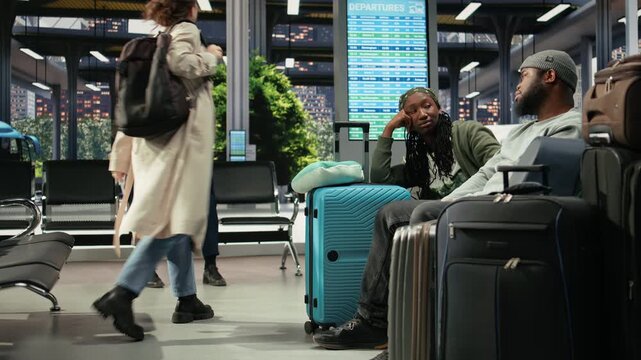 Exhausted travel companions discuss route plans beside a suitcase in a bus station, talking in the shuttle terminal while waiting for their coach connection.