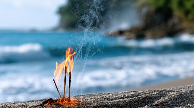 Burning incense sticks on sandy beach with ocean waves and blurred coastal background creating serene and peaceful outdoor atmosphere
