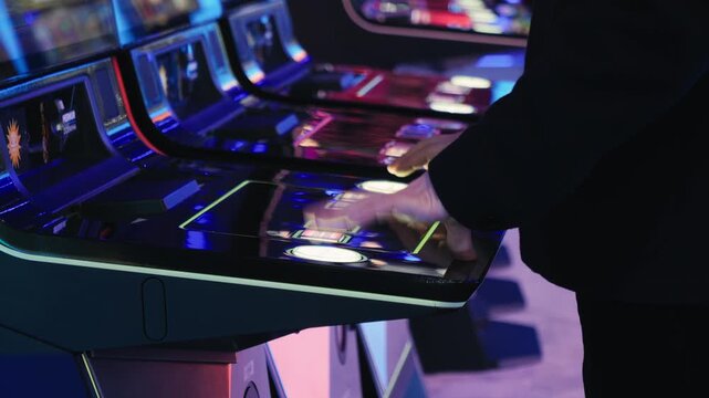 A man is playing slots machine and roulette or poker, gambling in casino close up, game machine in cafe or hotel lobby. Playing betting game.