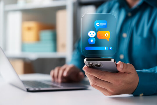A businessman uses a smartphone with a glowing AI chatbot hologram at his office desk. This modern virtual assistant interface represents smart communication and futuristic business technology.