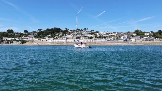 St Mawes Cornwall England UK. 13.08.2026. Video. A serene view of a sailboat moored in clear blue water with a charming white-washed village of St Mawes 