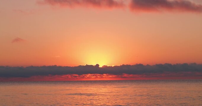 bright glowing sun behind dramatic clouds with light reflection on sea during scenic golden tropical sunrise