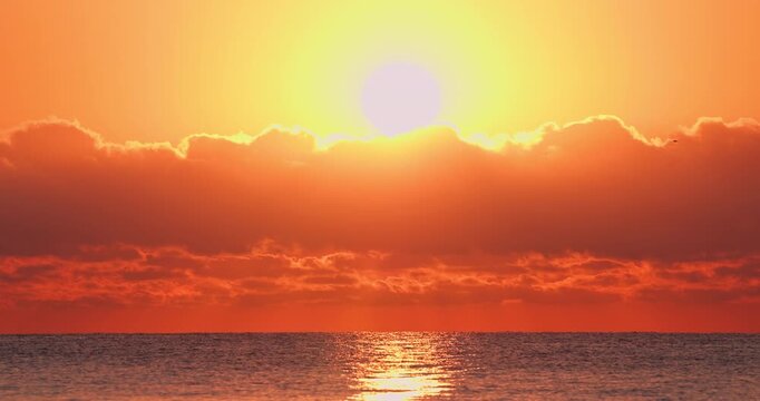 Bright glowing sun above dramatic clouds with light reflection on sea during scenic golden tropical sunrise