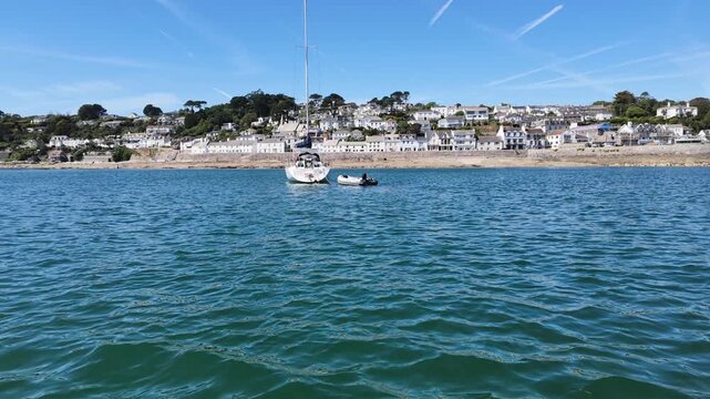 St Mawes Cornwall England UK. 13.08.2026. Video. A serene view of a sailboat moored in clear blue water with a charming white-washed village of St Mawes 