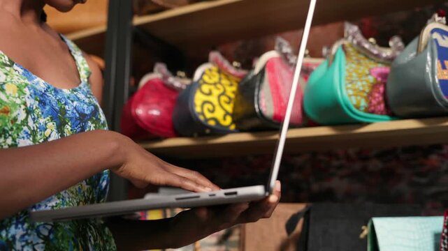 African woman operating a laptop, managing her small handbag business, SME
