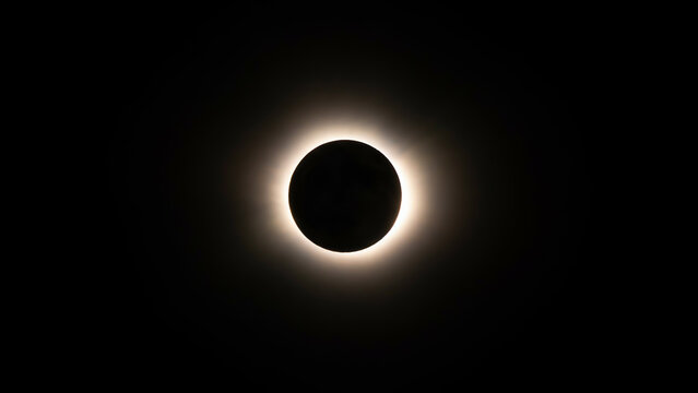 A long-exposure photograph of a total solar eclipse, showing the dark silhouette of the moon centered against the glowing corona of the sun