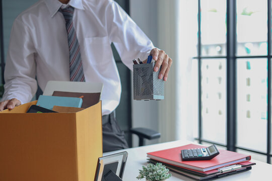 Office worker packing personal belongings into a cardboard box at a desk after job resignation or termination.
