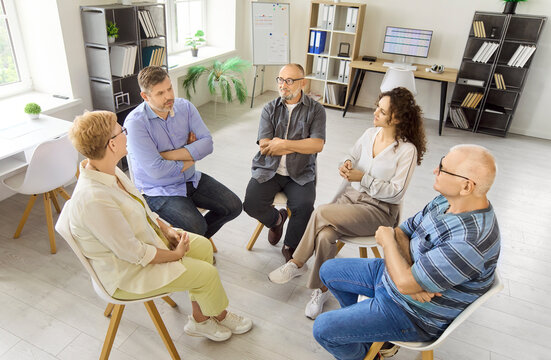 Adults seniors support group in therapy discussion. Mature adults sit in a circle, share, and listen during a counseling meeting in a community room. Concept of unity and mental wellbeing.