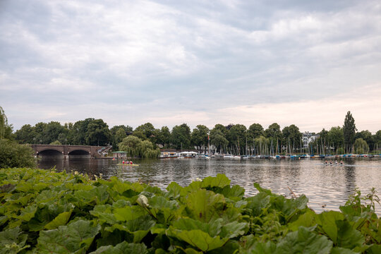 Arched stone bridge crossing an Alster waterway surrounded by lush summer vegetation in Hamburg, Germany.