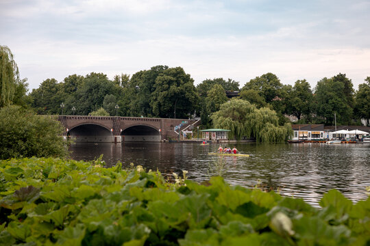 Arched stone bridge crossing an Alster waterway surrounded by lush summer vegetation in Hamburg, Germany.