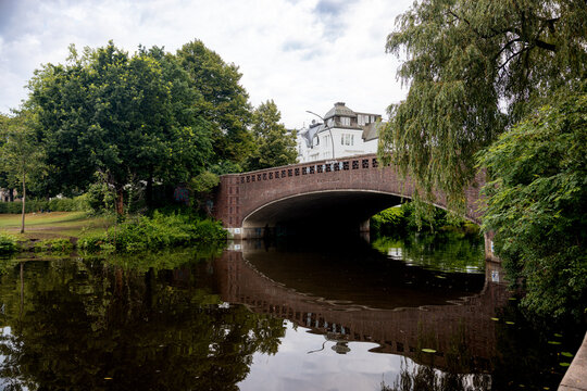 Arched stone bridge crossing an Alster waterway surrounded by lush summer vegetation in Hamburg, Germany.