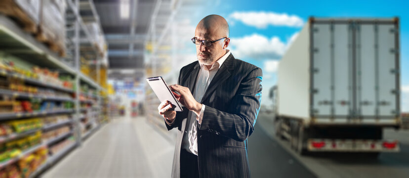 Retail supply logistics, manager uses tablet to coordinate food deliveries and transportation between distribution warehouse, store and cargo trucks.