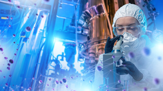 Biotechnology research, laboratory scientist uses microscope to analyze molecular samples and biological processes near industrial bioreactor equipment.
