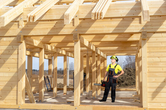 Wood framing construction. Builder operates chainsaw during house timber structure installation on residential building site.