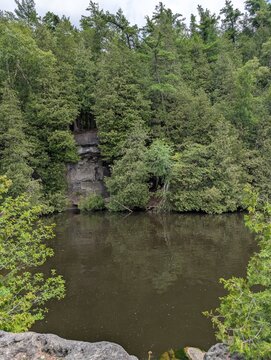 A park with beautiful conifers&mdash;cypresses and a lake whose waters flow past a rocky islands. A quiet, sunny day, with no people around. Rockwood&mdash;nature in the province of Ontario, Canada.