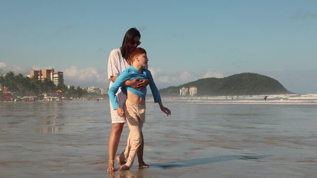 Caregiver helping a child use an all-terrain wheelchair near the ocean, showing accessible beach recreation, inclusion, mobility support and family care.