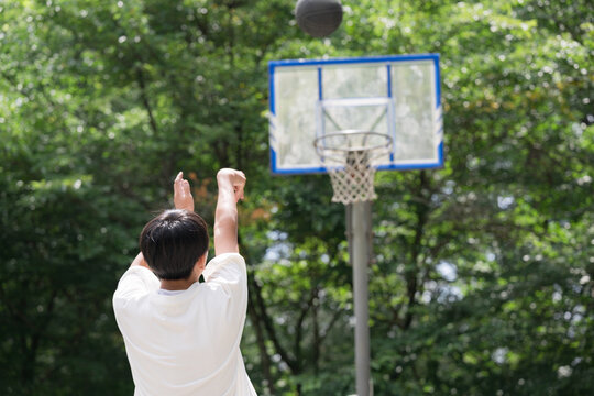 緑豊かな屋外コートでバスケットボールのシュートをする少年の後ろ姿の顔無し