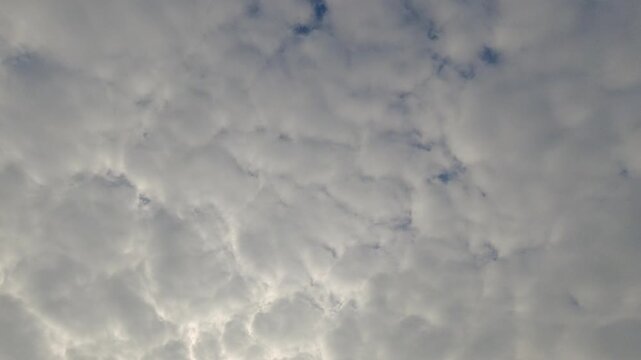 Dense white and grey clouds moving slowly across a bright sky. Beautiful overcast skyscape with soft natural lighting and small patches of blue. Perfect for weather and atmospheric backgrounds.