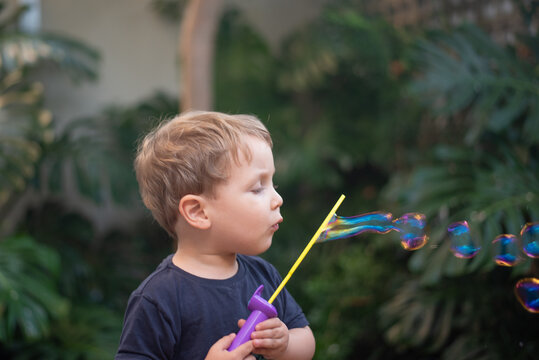 Two-year-old toddler boy blowing soap bubbles outdoors