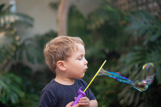 Two-year-old toddler boy blowing soap bubbles outdoors