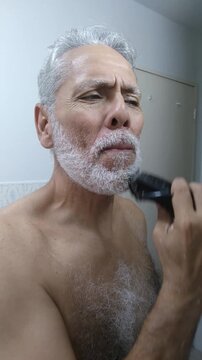 Mature man trimming and shaping his white beard and mustache with an electric clipper
